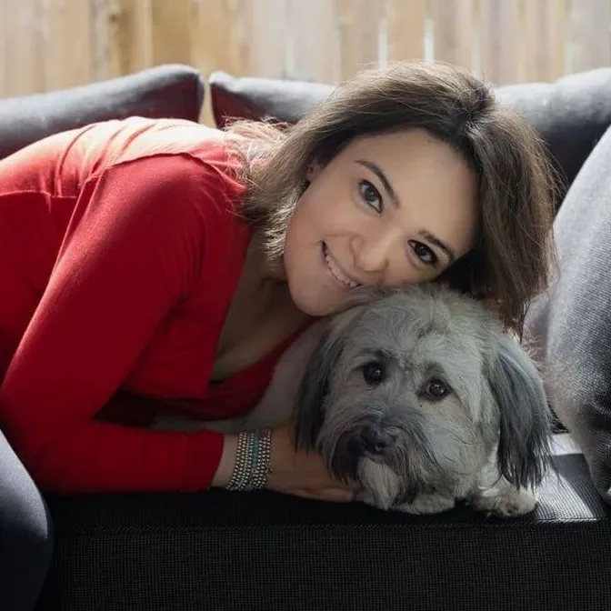 Woman in a red sweater hugging a havanese dog