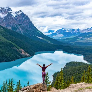 A woman posing with her hands in the air with a lake and the mountains in the background.