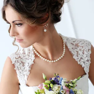 A wedding portrait of a brunette bride wearing pearls and holding a blue and pink bouquet of flowers.